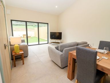 A living room with sofas television a dining table and glass doors leading to a garden at Bears Court Barn 3 Little Rissington near Bourton-On-The-Water