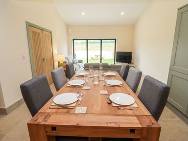 A dining table set with plates and glasses in a room with a sofa, TV, sliding glass doors and wooden double doors at Bears Court Barn 3 Little Rissington near Bourton-On-The-Water