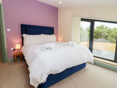 A bedroom with a bed bed with white bedding and towels on it a small lamp on a wooden side table and a large window at Bears Court Barn 3 Little Rissington near Bourton-On-The-Water