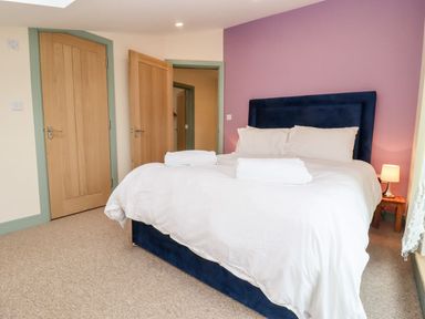 A bedroom with a bed with white linens and towels two wooden doors and a small lamp on a wooden side table at Bears Court Barn 3 Little Rissington near Bourton-On-The-Water