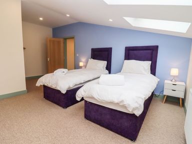 A bedroom with two single beds with white bedding and purple headboards and a bedside table with a lamp at Bears Court Barn 3 Little Rissington near Bourton-On-The-Water