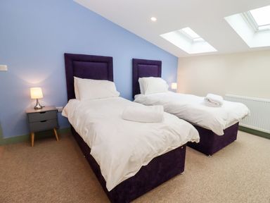 A bedroom with two single beds with white bedding and purple headboards a bedside table with a lamp skylight windows Bears Court Barn 3 Little Rissington near Bourton-On-The-Water