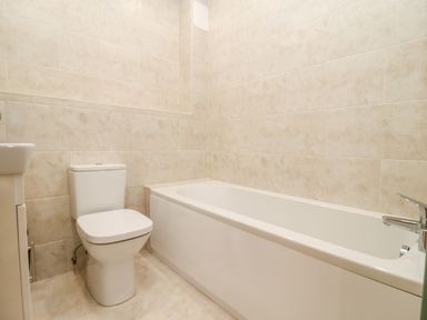 A bathroom with a bathtub a toilet and a tiled wall at Bears Court Barn 3 Little Rissington near Bourton-On-The-Water