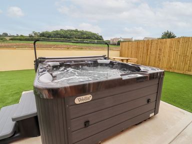 An outdoor hot tub in a yard with artificial grass and wooden fence at Bears Court Barn 3 Little Rissington near Bourton-On-The-Water
