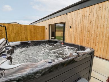 An outdoor hot tub next to a wooden fence and wooden building at Bears Court Barn 3 Little Rissington near Bourton-On-The-Water