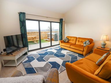 A living room with orange sofas a blue and gray geometric rug a television and sliding glass doors at Bears Court Barn 4 Little Rissington near Bourton-On-The-Water