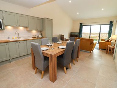 An open plan kitchen and dining area with wooden table and grey chairs next to a lounge with orange sofas at Bears Court Barn 4 Little Rissington near Bourton-On-The-Water
