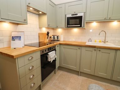 A kitchen with green cabinets wooden countertops an oven toaster knife block and a sink at Bears Court Barn 4 Little Rissington near Bourton-On-The-Water