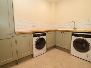A utility room with a washing machine and dryer under a wooden countertop and a sink at Bears Court Barn 4 Little Rissington near Bourton-On-The-Water