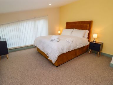 A bedroom with a double bed with white bedding two bedside tables with lamps and a window with vertical blinds at Bears Court Barn 4 Little Rissington near Bourton-On-The-Water