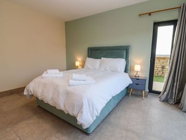 A bedroom with a bed white bedding folded towels bedside table lamps and a door with curtains at Bears Court Barn 4 Little Rissington near Bourton-On-The-Water