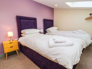 A bedroom with two single beds with purple headboards and white bedding next to a yellow bedside table with a lamp at Bears Court Barn 4 Little Rissington near Bourton-On-The-Water