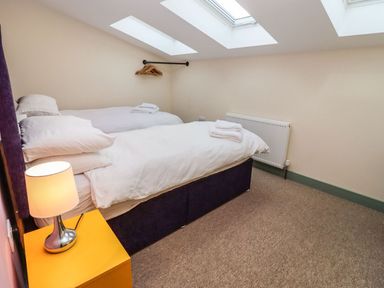 A bedroom with two single beds a yellow nightstand with a lamp wall-mounted radiator and skylight windows at Bears Court Barn 4 in Little Rissington near Bourton-On-The-Water