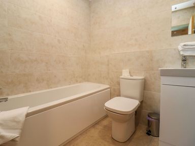 A bathroom with a bathtub a toilet a sink with towels and a trash can at Bears Court Barn 4 in Little Rissington near Bourton-On-The-Water