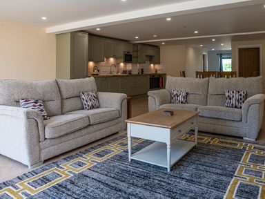 A living room with two gray sofas a wooden coffee table and a kitchen with green cabinets in the background at Bears Court Barn 7 Little Rissington near Bourton-On-The-Water