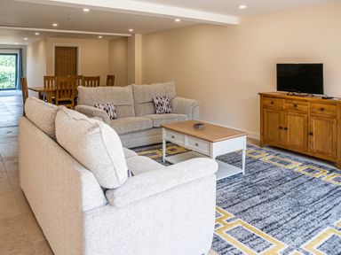 A living room with two sofas a coffee table a wooden TV stand with a television and a dining table with chairs at Bears Court Barn 7 Little Rissington near Bourton-On-The-Water