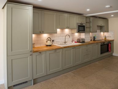 A kitchen with green cabinets wooden countertops a kettle toaster microwave oven and sink at Bears Court Barn 7 Little Rissington near Bourton-On-The-Water