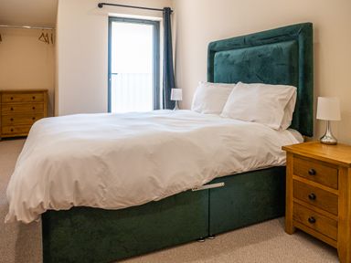 A bedroom with a bed with white bedding and a green headboard next to wooden bedside tables with lamps at Bears Court Barn 7 Little Rissington near Bourton-On-The-Water