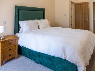 A bedroom with a bed with white bedding a wooden bedside table with a lamp and wooden doors at Bears Court Barn 7 in Little Rissington near Bourton-On-The-Water