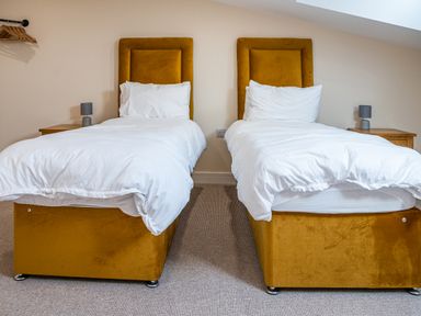 A bedroom with two single beds with yellow headboards and white bedding at Bears Court Barn 7 in Little Rissington near Bourton-On-The-Water