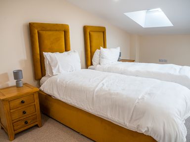 A bedroom with two single beds with mustard yellow headboards and white bedding a wooden bedside table and a skylight window at Bears Court Barn 7 in Little Rissington near Bourton-On-The-Water
