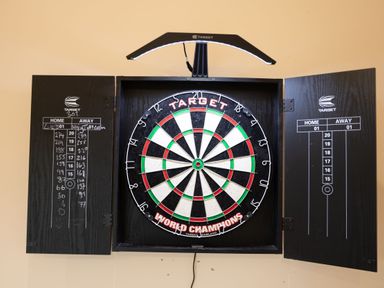 A dartboard mounted on a wall with open black cabinet doors displaying scoreboards at Bears Court Barn 8 Little Rissington near Bourton-On-The-Water