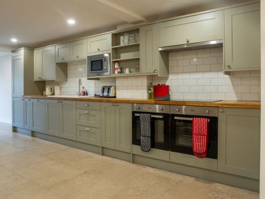 A kitchen with green cabinets wooden countertops two ovens a microwave toaster and kettle at Bears Court Barn 8 in Little Rissington near Bourton-On-The-Water