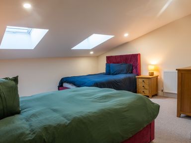 A bedroom with two beds with green and blue bedding under skylight windows at Bears Court Barn 8 in Little Rissington near Bourton-On-The-Water