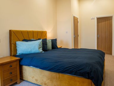 A bedroom with a bed with blue duvet and pillows and wooden side tables at Bears Court Barn 8 in Little Rissington near Bourton-On-The-Water