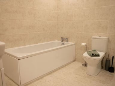 A bathroom with a bathtub a toilet with towels on the seat and a toilet paper holder Bears Court Barn 8 Little Rissington near Bourton-On-The-Water