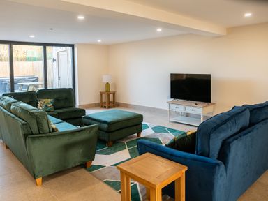 A living room with green and blue sofas a wooden side table and a television on a TV stand at Bears Court Barn 5 Little Rissington near Bourton-On-The-Water