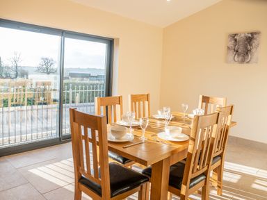 A dining room with a wooden table set with bowls, plates, glasses, and cutlery near sliding glass doors at Bears Court Barn 5 Little Rissington near Bourton-On-The-Water