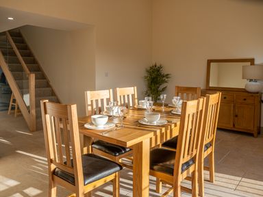 A dining room with a wooden table and six chairs set with plates bowls and glasses at Bears Court Barn 5 Little Rissington near Bourton-On-The-Water