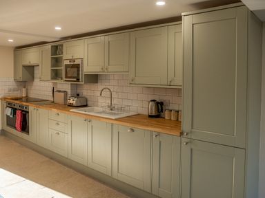 A kitchen with green cabinets a wooden countertop a sink kettle toaster microwave and oven at Bears Court Barn 5 Little Rissington near Bourton-On-The-Water