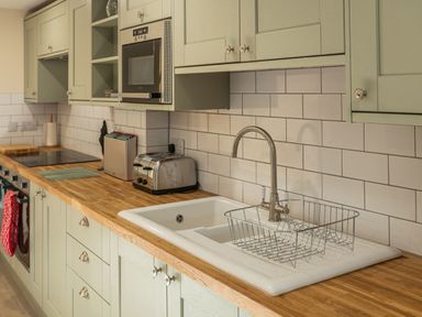 A kitchen with wooden countertop a white sink with metal dish rack green cabinets stainless steel toaster and microwave at Bears Court Barn 5 Little Rissington near Bourton-On-The-Water