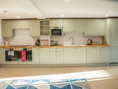 A kitchen with light green cabinets wooden countertops a stove two ovens a sink and various kitchen appliances at Bears Court Barn 5 Little Rissington near Bourton-On-The-Water