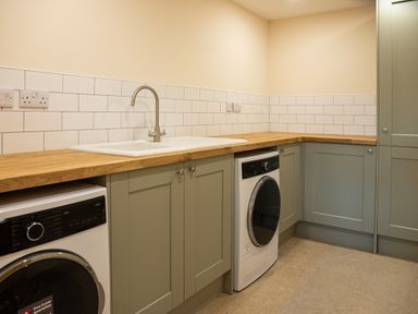 A utility room with a sink wooden countertops washing machine and dryer at Bears Court Barn 5 Little Rissington near Bourton-On-The-Water