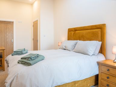 A bedroom with a double bed with folded towels on it wooden doors and bedside tables with lamps at Bears Court Barn 5 in Little Rissington near Bourton-On-The-Water