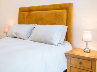 A bed with white pillows and bedding with a brown headboard and two bedside tables with lamps at Bears Court Barn 5 in Little Rissington near Bourton-On-The-Water