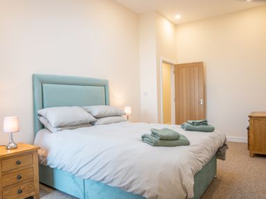 A bedroom with a double bed with green headboard and folded towels on the bed at Bears Court Barn 5 in Little Rissington near Bourton-On-The-Water