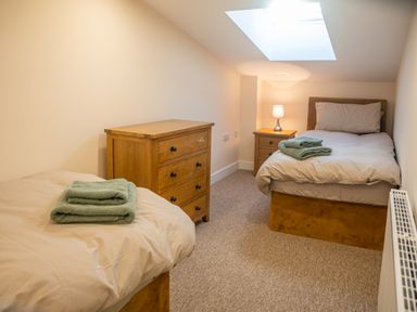 A bedroom with two single beds a wooden chest of drawers a bedside table with a lamp and skylight window at Bears Court Barn 5 in Little Rissington near Bourton-On-The-Water