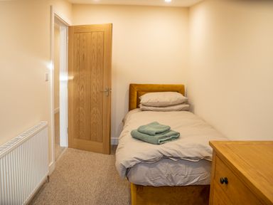 A small bedroom with a single bed with pillows and folded towels a wooden door radiator and wooden chest of drawers at Bears Court Barn 5 Little Rissington near Bourton-On-The-Water