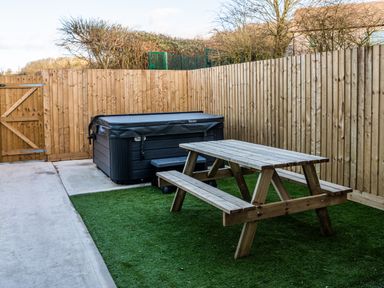 A backyard with a wooden picnic table and a hot tub along a wooden fence