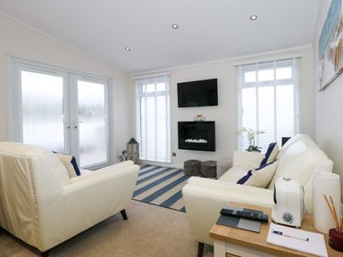 A living room with white sofas a wall-mounted TV and a fireplace at Un Diwrnod One Day The Warren T22 The Warren near Abersoch
