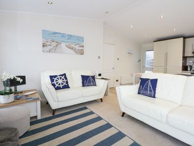 A living room with white sofas and blue nautical cushions at Un Diwrnod The Warren T22 The Warren near Abersoch