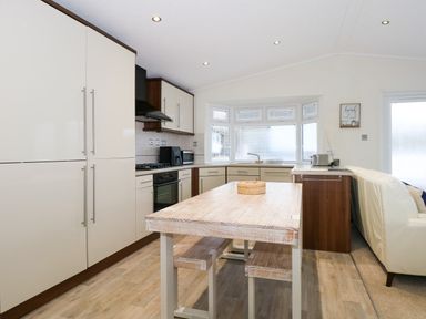 A kitchen with a wooden table and benches cabinets appliances and a window at Un Diwrnod The Warren T22 The Warren near Abersoch