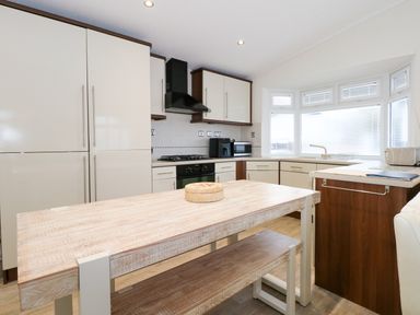 A kitchen with a wooden table bench seating cabinets appliances and a large window at Un Diwrnod One Day The Warren T22 The Warren near Abersoch