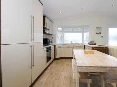 A kitchen with white cabinets a wooden table and bench seating by a window at Un Diwrnod The Warren T22 The Warren near Abersoch