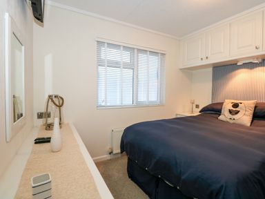 A bedroom with a bed with a sheep pillow and blue bedding and a window with blinds at Un Diwrnod The Warren T22 The Warren near Abersoch