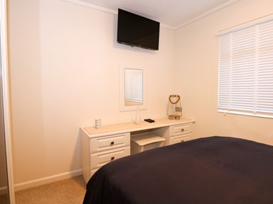 A bedroom with a wall mounted television a white dresser a small mirror and a window with blinds at Un Diwrnod (One Day) The Warren T22 The Warren near Abersoch